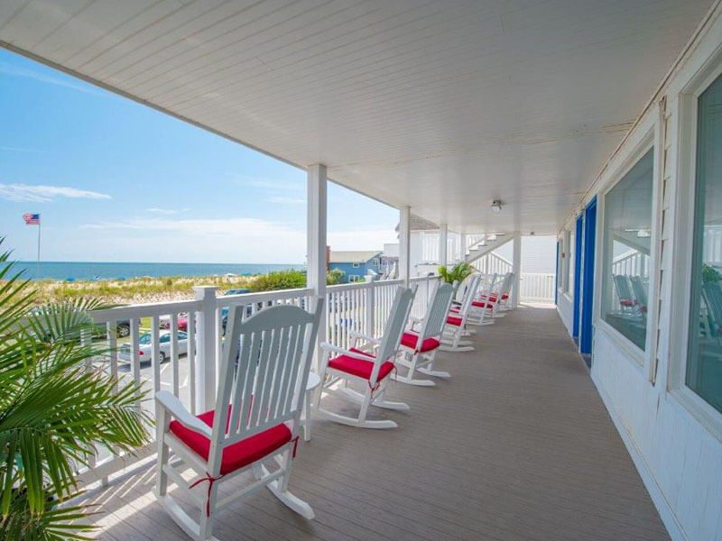 A full shot of the porch view with white chairs with red cushions on them along Dewey Beach.