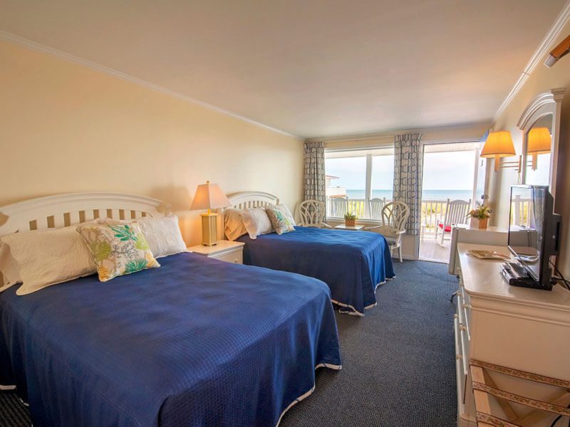 A full shot of a motel room with a twin bed with blue bed sheetaccess to porch.