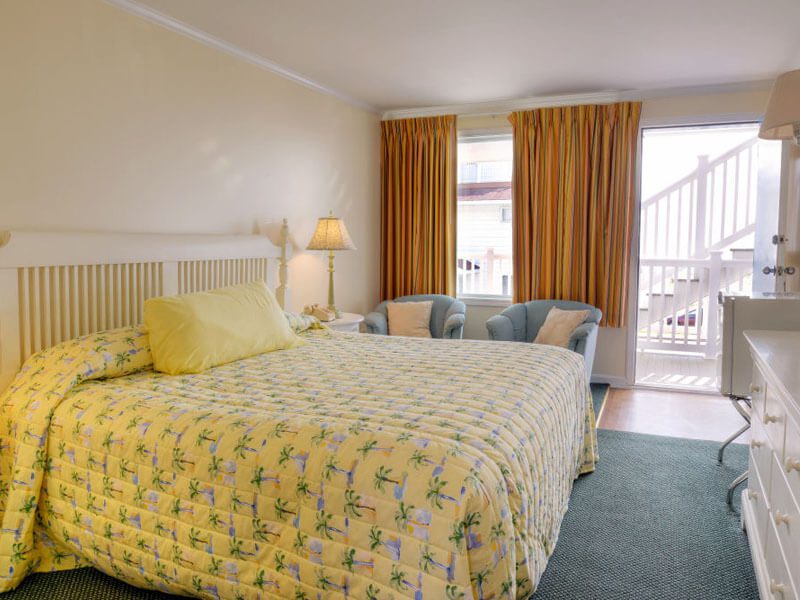 A full shot of a standard bed size ith yello bed sheet in motel room.